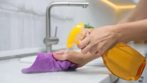 A woman cleans her white marble countertop with a rag and detergent.