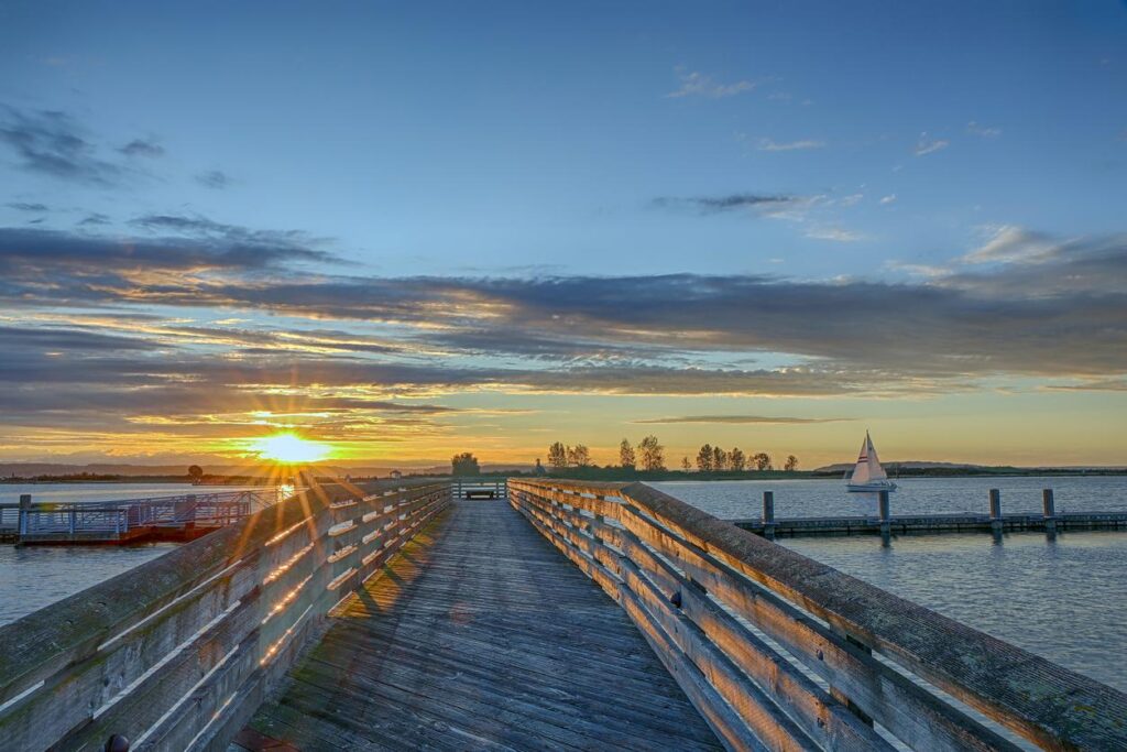 The sunsets over a pier in Everett, WA, with a sailboat in the background. 