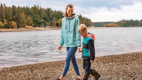 A mother and son walk lakeside on a cloudy day.