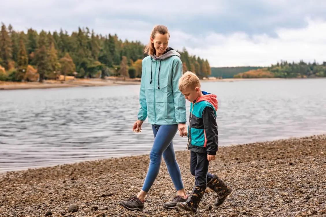 A mother and son walk lakeside on a cloudy day.