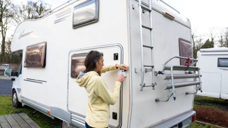 A woman in a yellow hoodie locking the rear door of a white camper van parked at an RV site during the daytime.