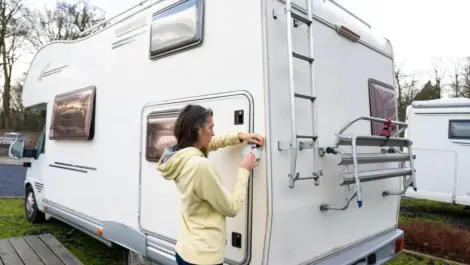 A woman in a yellow hoodie locking the rear door of a white camper van parked at an RV site during the daytime.
