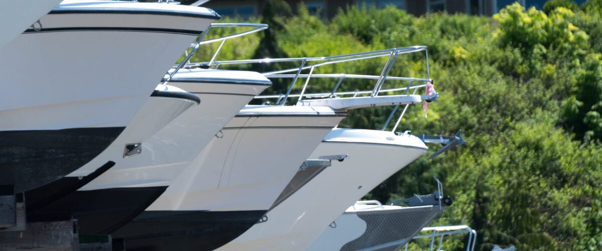 A row of boats stored outdoors with green trees and buildings behind them.