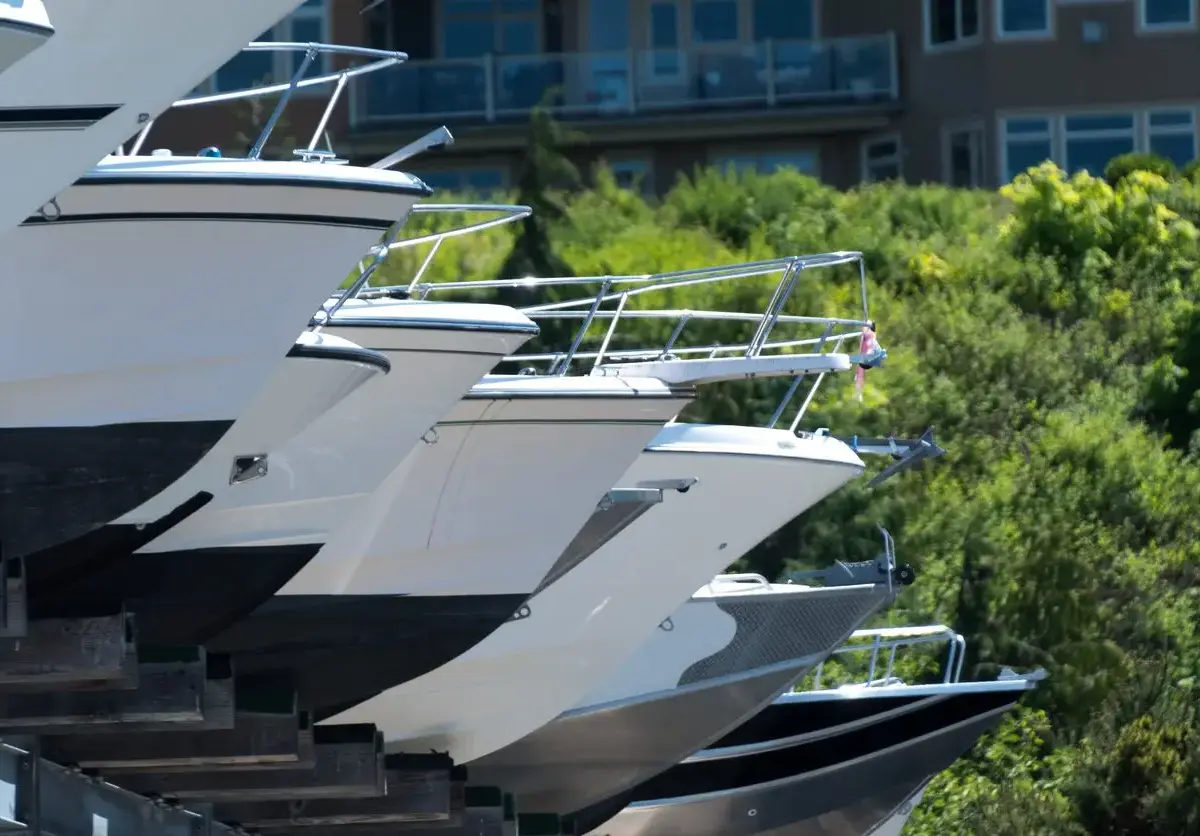 A row of boats stored outdoors with green trees and buildings behind them.