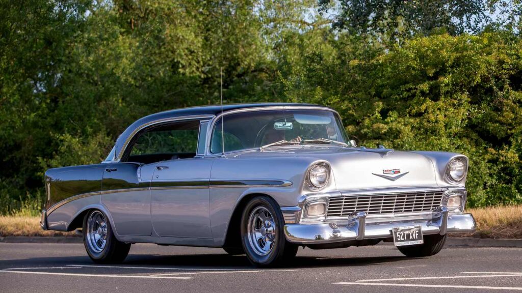 A silver, classic Chevrolet Bel Air out on a sunny day with trees in the background.