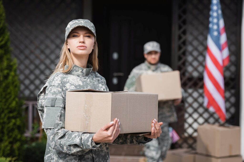 Military members holding moving boxes outside of a home.